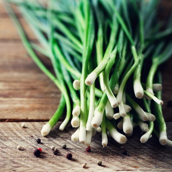Bunch of fresh organic green onions, scallions on wooden background with pepper